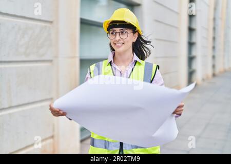 Giovane donna ispanica architetto lettura piani in strada Foto Stock