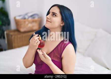 Giovane donna caucasica sorridente fiduciosa usando profumo in camera da letto Foto Stock