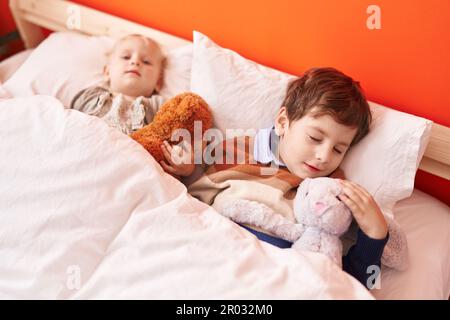Adorabile ragazzo e ragazza che abbraccia orsacchiotto che dorme a letto in camera da letto Foto Stock