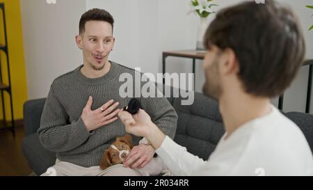 Due uomini sorridono fiduciosi sorpresa con la proposta di fidanzamento a casa Foto Stock