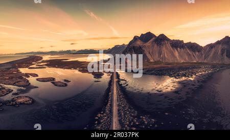 Panorama vista aerea di bella alba sul monte Vestrahorn vichingo villaggio e strada tra spiaggia di sabbia nera a Stokksnes in estate in Islanda Foto Stock