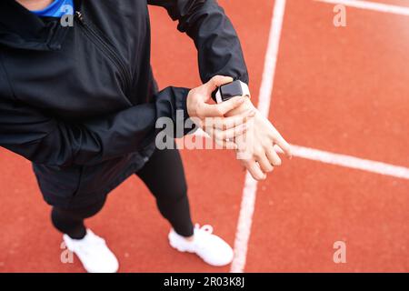 Atleta donna in piedi su piste da corsa e utilizzando il suo orologio da polso digitale. Foto Stock