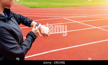 Atleta donna runner in piedi sulle piste da corsa e utilizzando il suo orologio da polso digitale. Foto Stock