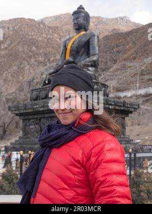Saccopelatore femmina a Muktinath, Nepal, che smilling con fiducia con enorme Buddha di pietra sullo sfondo. Foto Stock