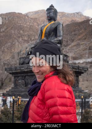 Zaino in spalla femmina a Muktinath, Nepal, silling sneaky con enorme Buddha di pietra sullo sfondo. Foto Stock