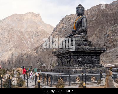 Vista orizzontale di una donna zaino in spalla a Muktinath, Nepal, in preghiera a Namaste mudra di enorme Buddha di pietra. Foto Stock