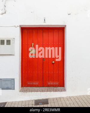 Porta in legno rosso. Parete bianca dell'edificio, portiere dorate, marciapiede piastrellato, fili sulla parete, numero civico. Foto di alta qualità Foto Stock