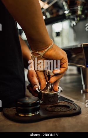 Un barista sta assottigliando il caffè appena macinato in un portafiltro prima della preparazione Foto Stock