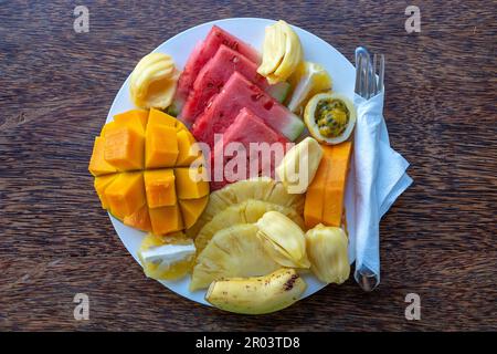 Frutta tropicale su un piatto da colazione, primo piano. Anguria fresca, banana, frutto della passione, ananas, jackfruit, mango, papaya, arancia per mangiare in bea Foto Stock