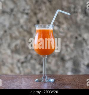 Spremuta fresca di frutta tropicale in un calice di vetro sullo sfondo di un vecchio muro di pietra. Isola di Zanzibar, Tanzania, Africa orientale. Chiudi Foto Stock