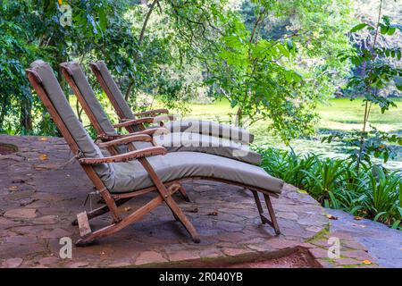 Tre comodi lettini sulla terrazza con giardino tropicale vicino al lago. Tanzania, Africa orientale, primo piano Foto Stock