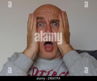 Ritratto dell'uomo preoccupato e spaventato con le mani sul viso, isolato su sfondo bianco, maschio calvo, occhi blu Foto Stock