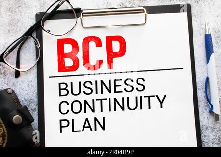 Su un tavolo da ufficio di colore chiaro si trova un computer, una calcolatrice nera, una penna e un notebook con il testo BCP Business Continuity Plan Foto Stock