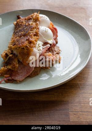 Viziatevi con questo delizioso e accogliente brunch che unisce frittelle di patate croccanti, uova in camicia e pancetta croccante. La cottura a vapore è calda Foto Stock