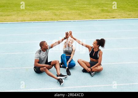 L'abbiamo fatto. Ripresa completa di un gruppo di atleti che si siedono e si danno a vicenda un alto cinque dopo la corsa. Foto Stock