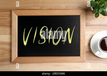 Piccola lavagna con parola visione, caffè e pianta su tavolo di legno, piatto Foto Stock