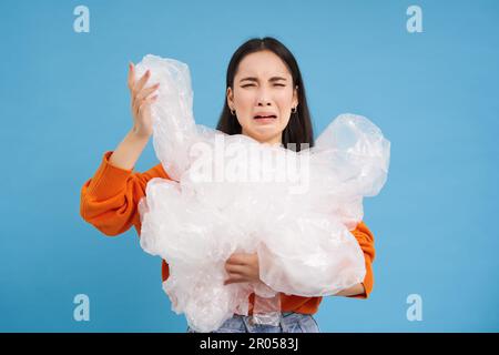 Donna asiatica piangente con rifiuti di riciclaggio di plastica, stanco di smistamento rifiuti in diversi contenitori, preservando la natura, sfondo blu. Foto Stock