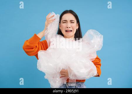 Donna asiatica piangente con rifiuti di riciclaggio di plastica, stanco di smistamento rifiuti in diversi contenitori, preservando la natura, sfondo blu Foto Stock