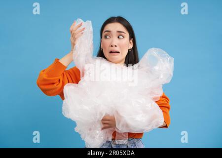 Donna asiatica piangente con rifiuti di riciclaggio di plastica, stanco di smistamento rifiuti in diversi contenitori, preservando la natura, sfondo blu Foto Stock