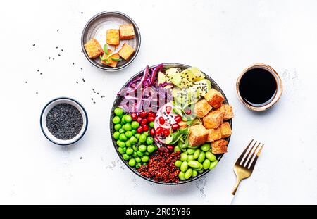Cibo vegano sano. Ciotola di Buddha con quinoa, tofu fritto, avocado, edamame, piselli verdi, ravanello, cavolo e semi di sesamo. Backgroun tavolo da cucina bianco Foto Stock