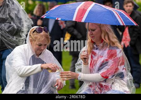 Le femmine celebrano l'incoronazione di Re Carlo III ad Hyde Park con un drink, al riparo sotto un ombrello sotto la pioggia. Foto Stock