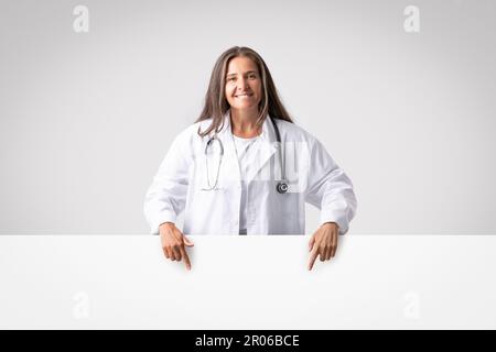Grande offerta medica. Donna felice del medico anziano che indica giù al bordo libero di pubblicità con lo spazio vuoto per il disegno Foto Stock