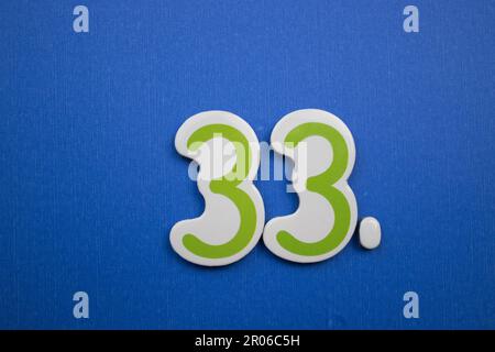 Il numero 33, posto su uno sfondo blu, fotografato dall'alto, è di colore verde e blu scuro. Foto Stock
