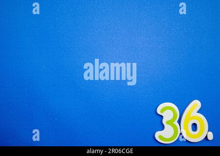 Il numero 36, verde e giallo, fotografato dall'alto, posto sul bordo di uno sfondo blu. Foto Stock