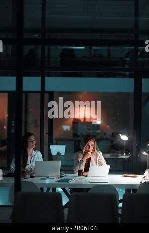 La prova è nella dedizione. due colleghi che utilizzano i loro computer portatili durante una notte tarda in un ufficio moderno. Foto Stock