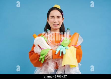 Donna asiatica piangente con bottiglie di plastica vuote, usato guanti in lattice sporco, grida sul riciclaggio, smista rifiuti, sfondo blu Foto Stock