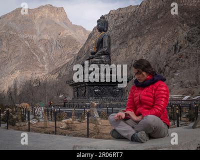 Saccopelatore femmina a Muktinath, Nepal, praticando shiatsu con se stessa e Buddha di pietra enorme sullo sfondo. Foto Stock