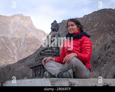 Saccopelatore femmina a Muktinath, Nepal, meditando con enorme Buddha di pietra sullo sfondo. Foto Stock