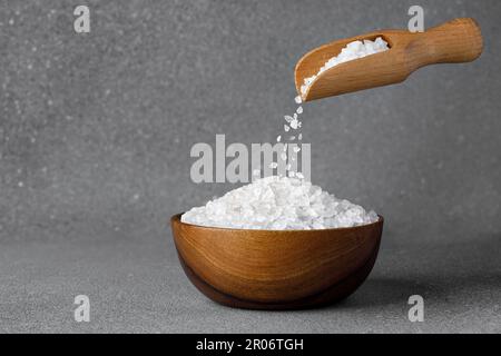 cristalli di sale marino che cadono dalla paletta in ciotola su fondo grigio Foto Stock