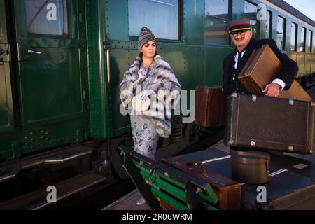 Scena di rievocazione sulla piattaforma vicino a un autentico vagone ferroviario di prima classe 1927 dove una donna di lusso 1920s sta aspettando il suo bagaglio Foto Stock