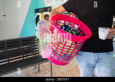 Primo piano di un cesto con vestiti da lavare tenuti da un uomo nella lavanderia Foto Stock