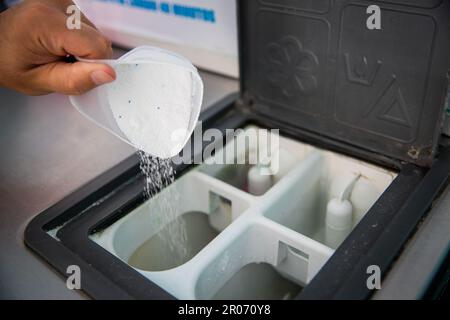 Primo piano delle mani di un uomo che versa detersivo in polvere in lavatrice nella lavanderia Foto Stock