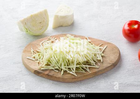 Asse di legno con cavolo grattugiato su fondo grigio chiaro. Cucinare cibi vegani sani Foto Stock