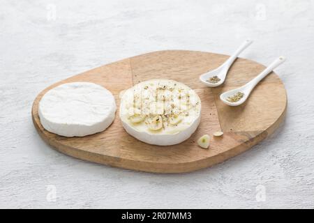 Pannello di legno con testa tagliata di formaggio bianco, aglio tritato e spezie su sfondo grigio chiaro. Fase di cottura di un delizioso spuntino di vacanza Foto Stock
