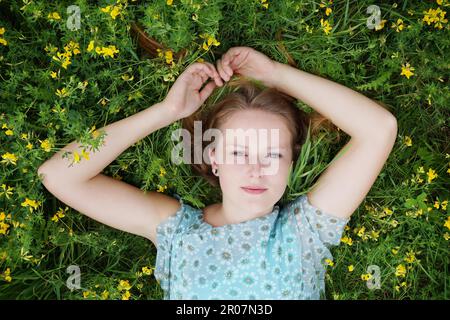 Giovane donna giacente in un prato di fiori godendo di dolce far niente Foto Stock