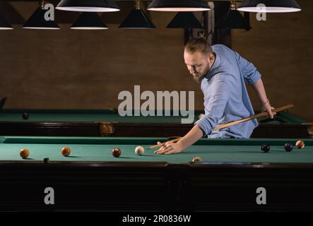 uomo caucasico concentrato in abiti casual giocando a biliardo. preparatevi a colpire la palla. banner. Foto Stock