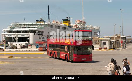 Porto di Heraklion, Creta, Grecia, UE. 2023. Autobus rosso per tour della città con tetto aperto al porto di Heraklion con traghetto roro e passeggeri in attesa lungo la banchina Foto Stock