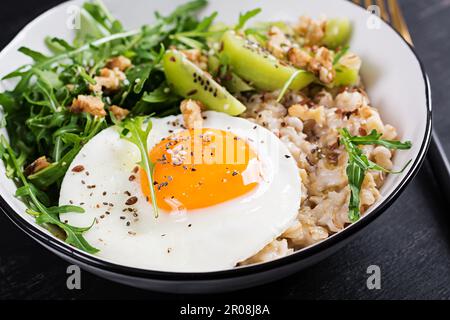 Porridge di farina d'avena con uova arrosto, kiwi, rucola e semi di lino. Colazione sana per abbassare il colesterolo. Foto Stock