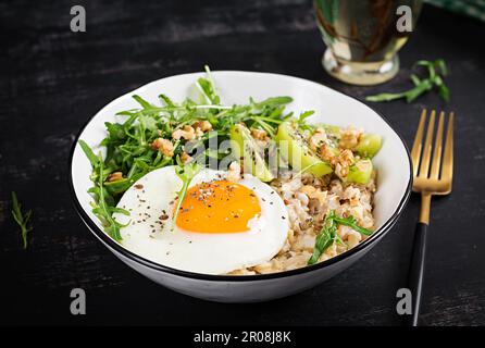 Porridge di farina d'avena con uova arrosto, kiwi, rucola e semi di lino. Colazione sana per abbassare il colesterolo. Foto Stock