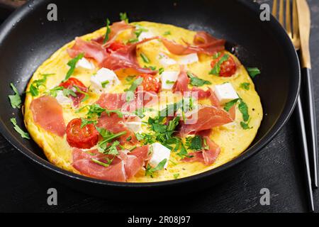 Omelette con pomodori, jamon e feta in padella. Foto Stock