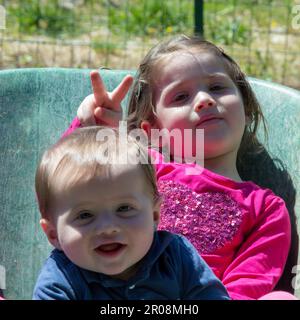 Immagine di due adorabili bambini sorridenti che si tengono all'interno di una carriola. Amore fraterno come giocano nel giardino con la loro sorella fare Foto Stock