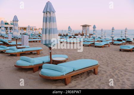 Lettini e ombrelloni vuoti su una spiaggia di sabbia vicino al mare Foto Stock