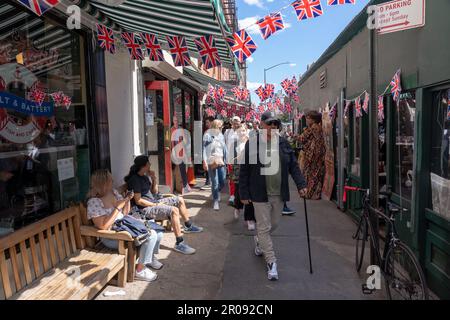 NEW YORK, NEW YORK - 6 MAGGIO: Pedoni a piedi decorato con bandiere Union Jack per celebrare l'incoronazione di sua Maestà Re Carlo III britannico di proprietà del ristorante tè & simpatia a Manhattans Greenwich Village il 6 maggio 2023 a New York City. L'incoronazione di Carlo III e sua moglie, Camilla, come Re e Regina del Regno Unito di Gran Bretagna e Irlanda del Nord, e gli altri regni del Commonwealth si svolge oggi presso l'Abbazia di Westminster. Carlo entrò in trono il 8 settembre 2022, alla morte di sua madre, Elisabetta II Foto Stock