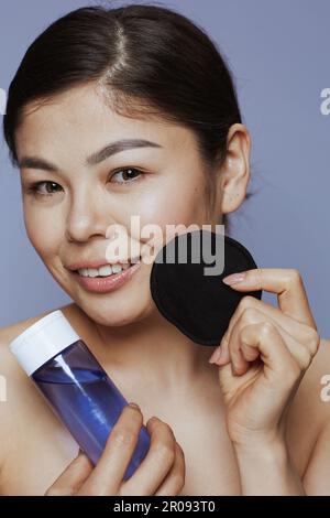 giovane donna asiatica con smacchiatore per il trucco e tampone di cotone nero su sfondo blu. Foto Stock