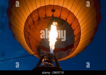 Un'inquadratura a basso angolo di una mongolfiera di colore arancione con i suoi comandi al fuoco Foto Stock