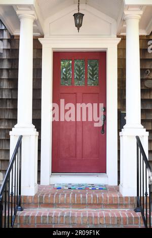 Una porta rossa su una casa con scandole di cedro e colonne bianche. Foto Stock